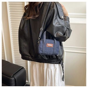 Detail of a retro blue denim mini pillow bag with white stitching and leather patch