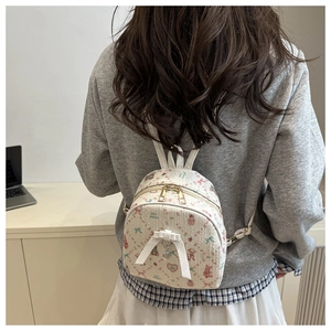 Détail d'un mini sac à dos blanc avec motifs cartoon, texture tissée et pendentif cœur