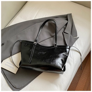 Detail of black glossy tote bag with silver hardware on grey blazer, 2025 office style