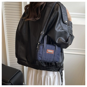 Detail of dark blue denim mini bag with contrast stitching and adjustable metal buckle strap