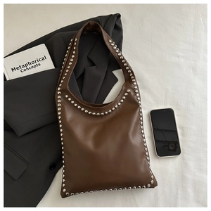 Detail of a brown leather tote bag with silver metal rivets on white fabric