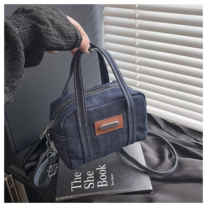 Detail of a dark blue denim handbag featuring contrast stitching and leather patch