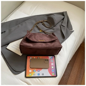 Close-up of deep brown suede crossbody bag with gold chain strap and metal bar detail