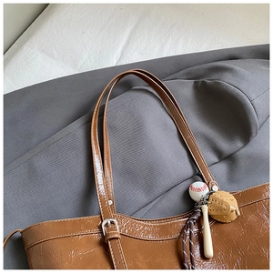 Detail of brown glossy leather tote bag with baseball charm and buckle on slim strap