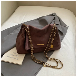 Close-up of a dark brown suede tote bag featuring a gold metal buckle and chain strap