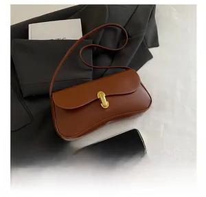 Detail view of brown leather underarm bag with gold metal buckle and phone for size reference