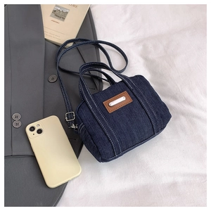 Detail of dark blue denim mini tote bag with white topstitching and metal plaque