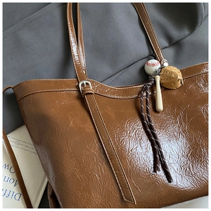Detail of a brown tote bag with glossy wrinkled texture and a baseball charm set