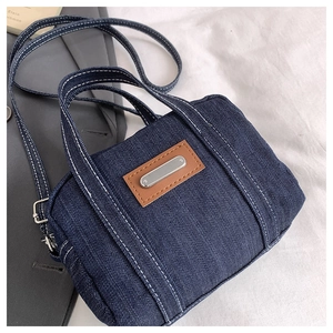 Detail of blue denim mini crossbody bag featuring white contrast stitching and metal plate