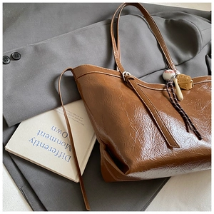 Detail of a brown glossy leather tote bag featuring a creative baseball glove charm