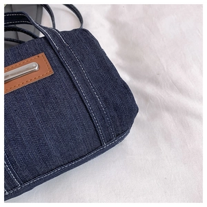 Close-up of dark denim handbag showing white contrast stitching and leather patch detail