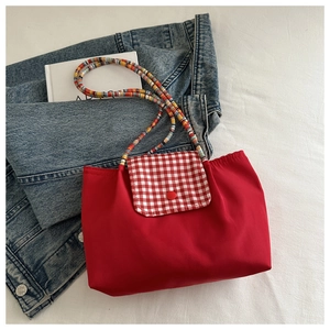 Détail du sac cabas rouge en nylon avec rabat à carreaux et bandoulière en perles colorées