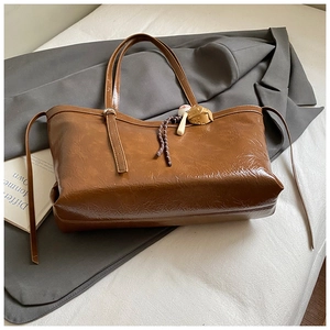 Detail of a brown tote bag featuring glossy wrinkled leather and a creative baseball pendant