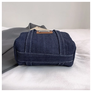 Detailed base view of deep blue denim handbag featuring contrast white stitching and leather trim