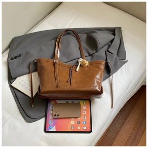 Detail of a brown oil-wax leather tote bag with a small baseball bat pendant and strap