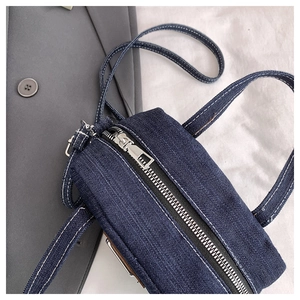 Detail of blue denim pillow bag showing silver zipper and white contrast stitching texture