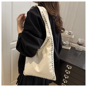 Detail of cream tote bag with silver studs worn by model in minimalist interior