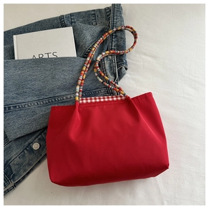 Détail du sac cabas rouge avec poignée tissée colorée et bordure à carreaux sur denim