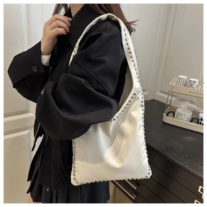Detail view of white leather shoulder bag with silver rivet studs on the side and bottom