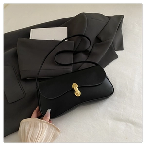 Minimalist black baguette bag with gold U-shaped lock on a dark grey blazer
