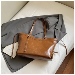 Detailed view of brown tote bag in oil wax leather with metallic buckle on a grey suit