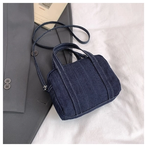 Macro detail of dark blue denim handbag with contrast white stitching on white fabric