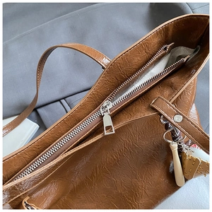 Detailed close-up of brown tote bag with wrinkled leather texture and baseball keychain