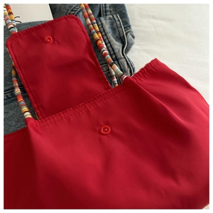 Détail du sac cabas en nylon rouge avec bandoulière rayée et fermeture à bouton-pression