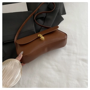 Close-up of minimalist brown leather baguette bag with a golden metallic twist lock