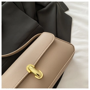 Detail of lychee pattern leather and gold metal buckle on a minimalist beige shoulder bag