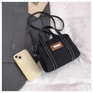 Detail of black denim handbag with white contrast stitching and metallic logo tag