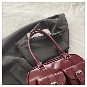 Detail of wine red glossy shoulder bag with dual buckle pockets and sleek patent finish