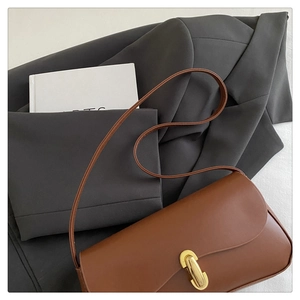 Detail of a brown leather baguette bag featuring an elegant oval golden metal buckle