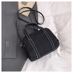 Detail of a black denim crossbody bag with contrast white stitching and top handles