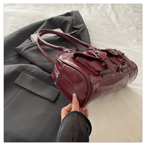 Detail of dark burgundy cylindrical shoulder bag featuring glossy finish and buckle pockets