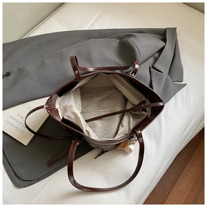 Macro view of a deep brown glossy tote bag showing spacious interior with baseball charm