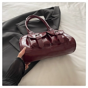 Detail of burgundy glossy leather shoulder bag with silver buckles and retro pockets