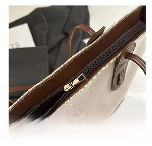 Detail of smooth gold metal zipper and brown leather trim on a canvas tote bag