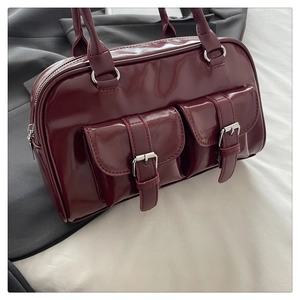 Close-up of a burgundy patent leather underarm bag with decorative front buckle pockets