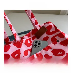 Detail view of pink leopard tote bag with a leather label pocket holding a phone
