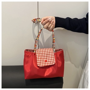 Détail du sac cabas en nylon rouge avec rabat à carreaux et poignée tressée colorée