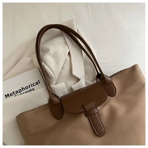 Dettaglio di una borsa tote in nylon marrone con manici in pelle su tessuto bianco