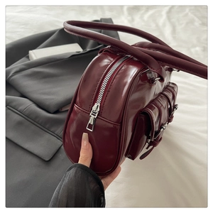 Detail of dark red patent leather shoulder bag with side buckle pockets and silver zipper