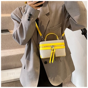 Detail of yellow and beige canvas box bag with tassels on a model with grey blazer