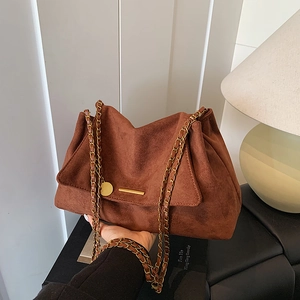 Brown suede tote bag with gold chain strap and minimalist metal bar accent in lifestyle view
