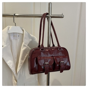 Detail of burgundy glossy oil-wax leather handbag featuring dual front buckle pockets
