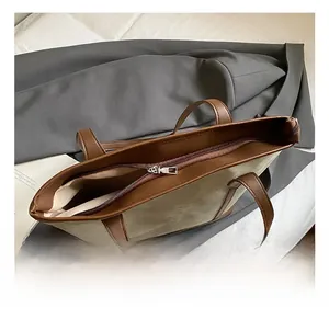 Detail of silver metal zipper and dual brown leather handles on a green tote bag