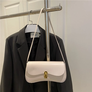 Minimalist beige leather underarm bag with gold metal clasp on a textured black suit