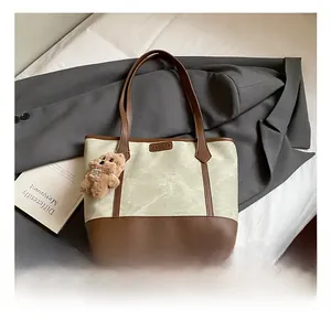 Detail showing the mixed canvas and leather texture with a cute bear charm on a tote bag