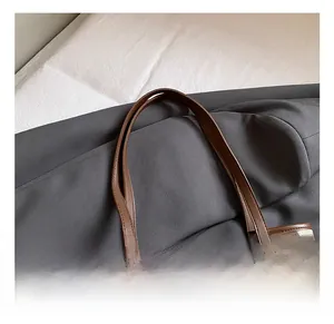 Detail of leather handles and canvas texture on a minimalist tote bag with charm